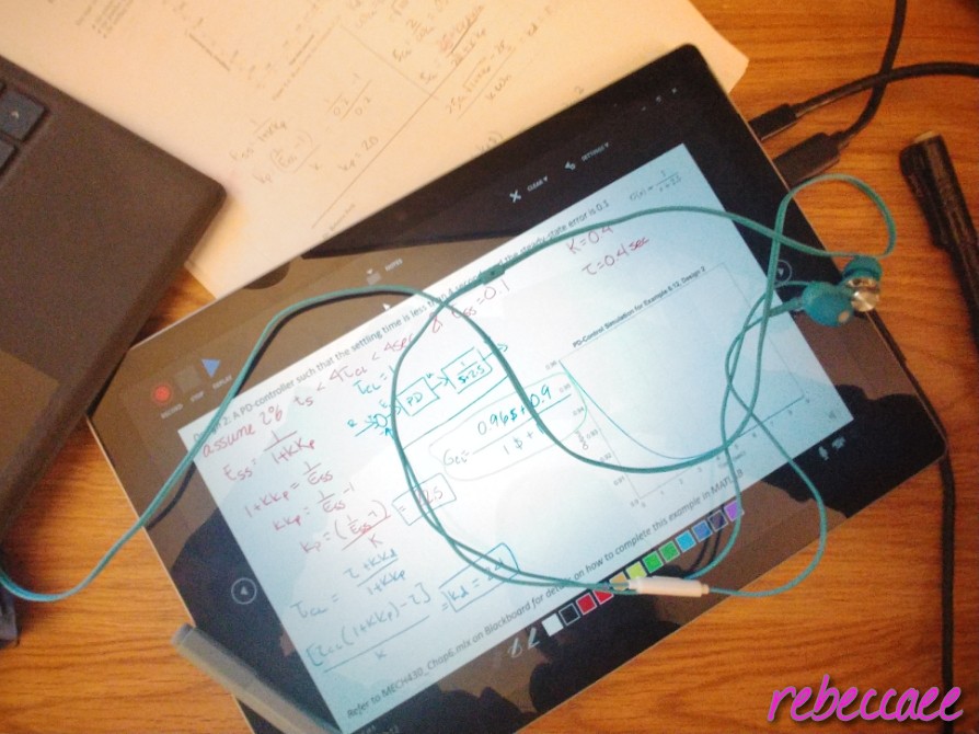 A computer tablet sitting on a desk with a pair of wired headphones.